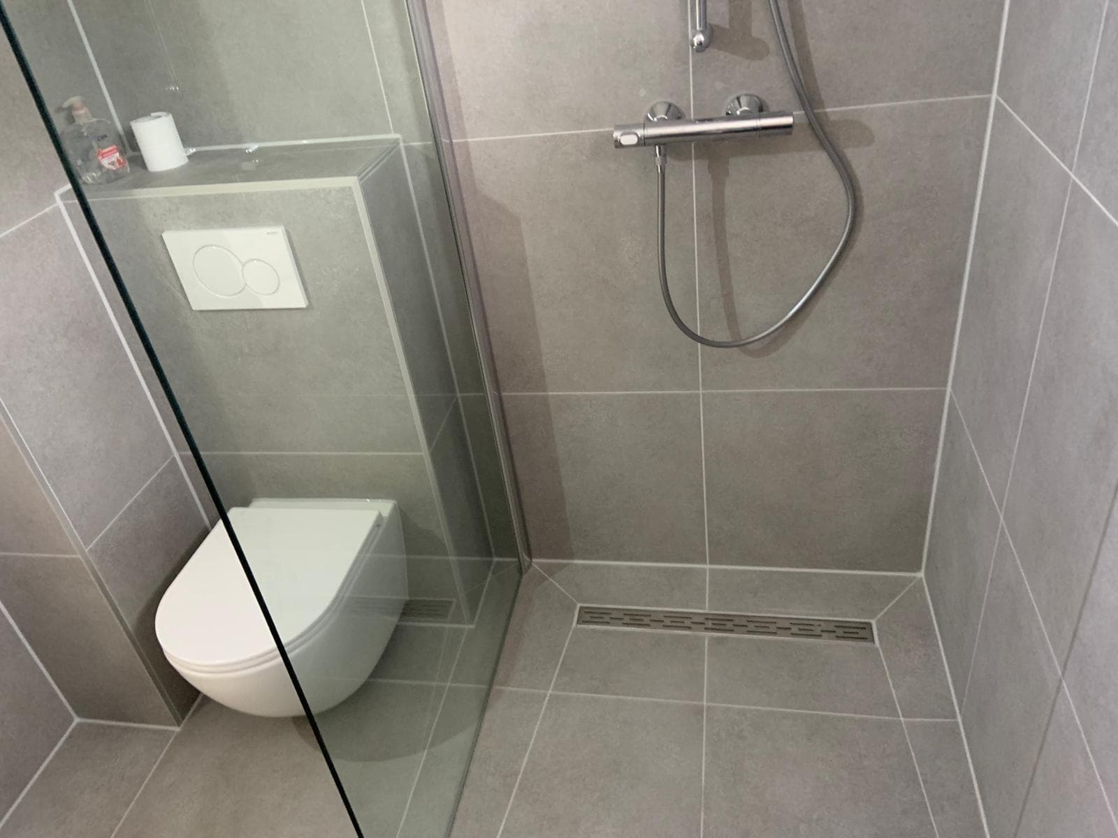 Inloopdouche met grijze wandtegels, lijnput en wandtoilet